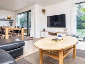 Un salon moderne avec une table à manger en bois, un canapé en cuir noir et un grand téléviseur à écran plat fixé au mur.