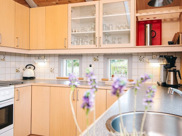 A kitchen with wooden cabinets, a kettle, a coffee maker, and a window with a view of greenery. - 4 Star Holiday Home in Henne (Henne)