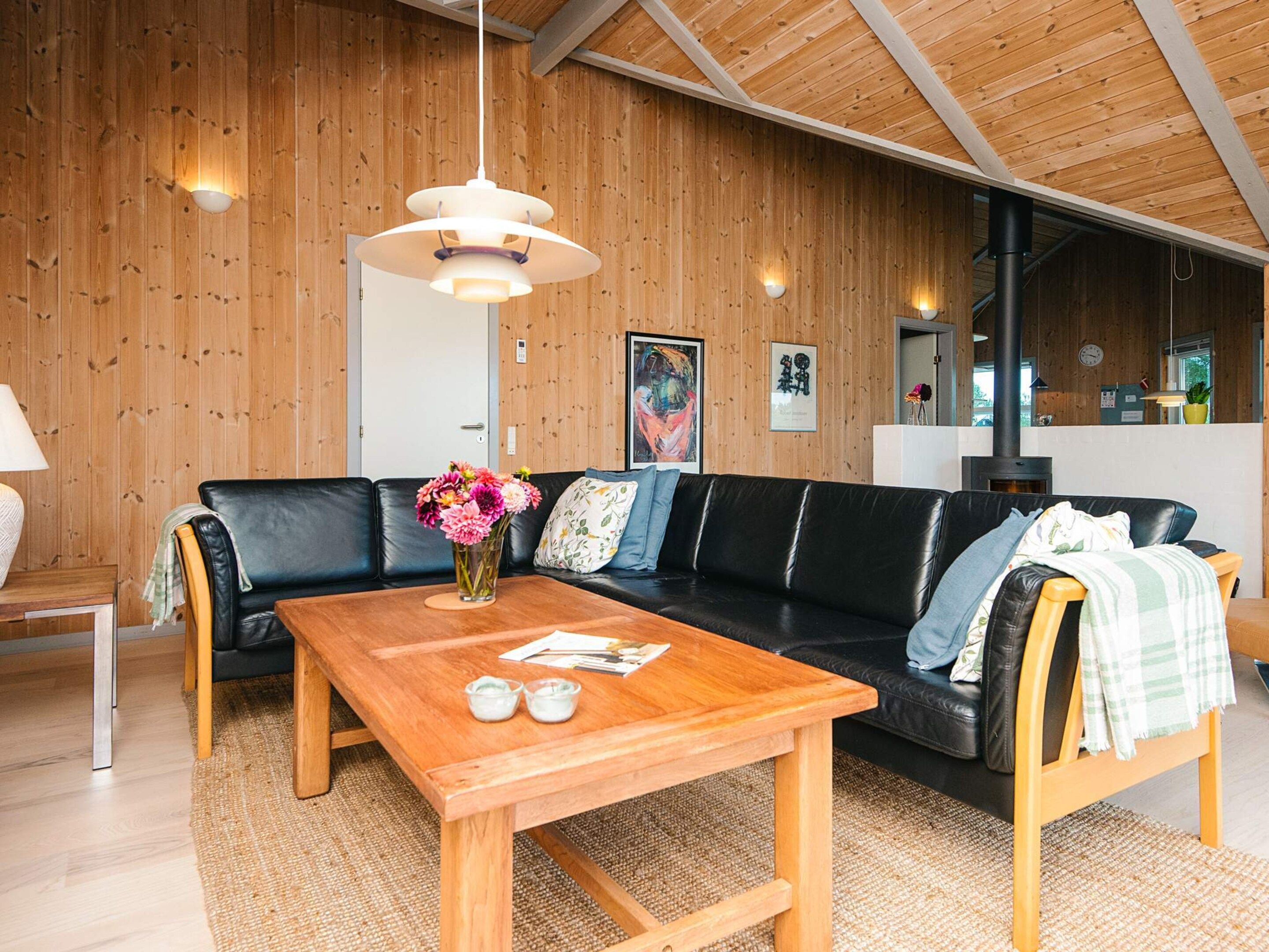 Ein modernes Wohnzimmer mit Holzboden, einem schwarzen Ledersofa, einem Couchtisch aus Holz und einem Blumenvasen.