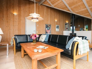 A modern living room with a wooden ceiling, a black leather sofa, a wooden coffee table, and a vase of flowers. - 4 Star Holiday Home in Henne (Henne)