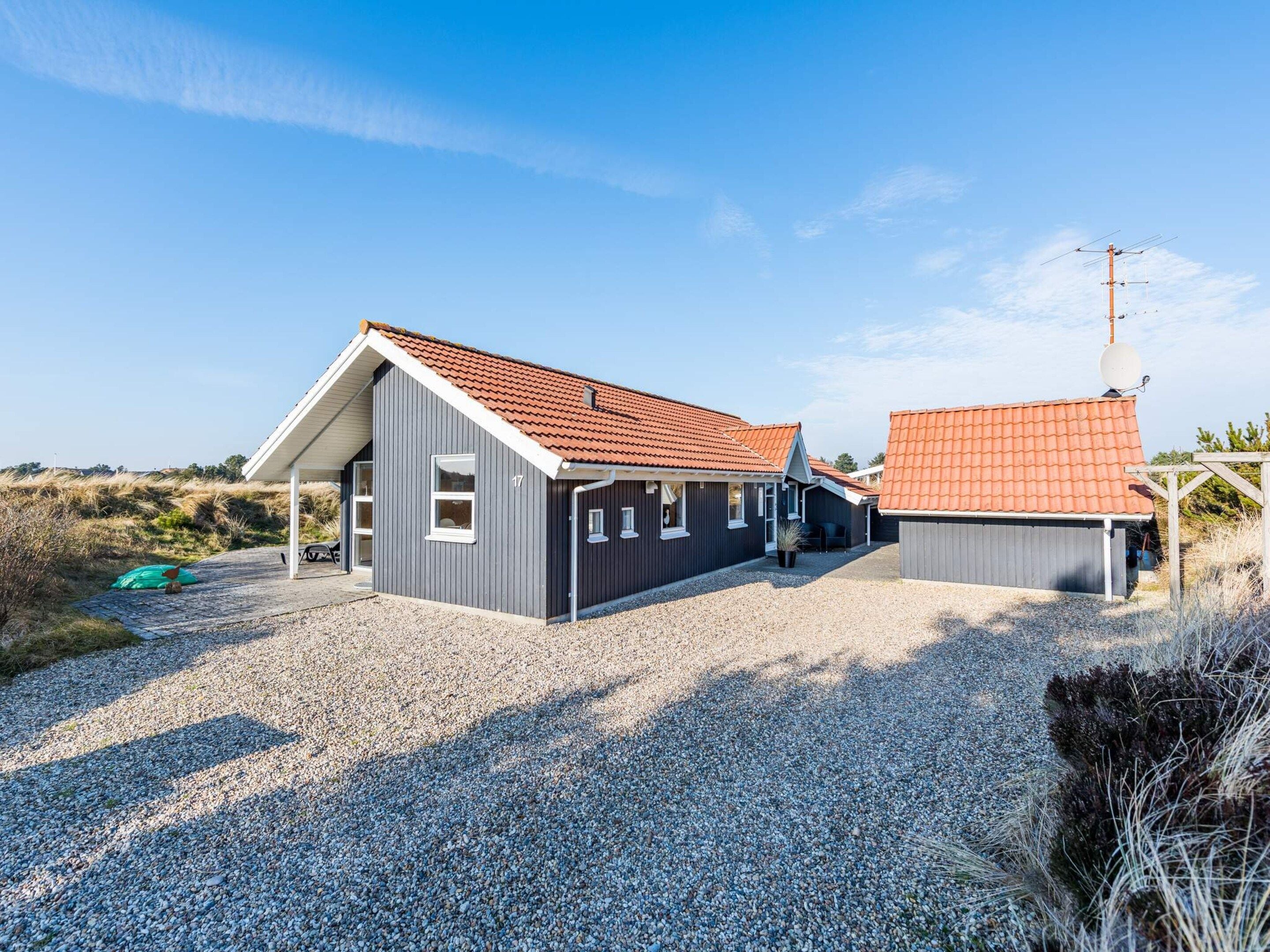 A two-story building with a red-tiled roof, a gravel driveway, and a clear blue sky.