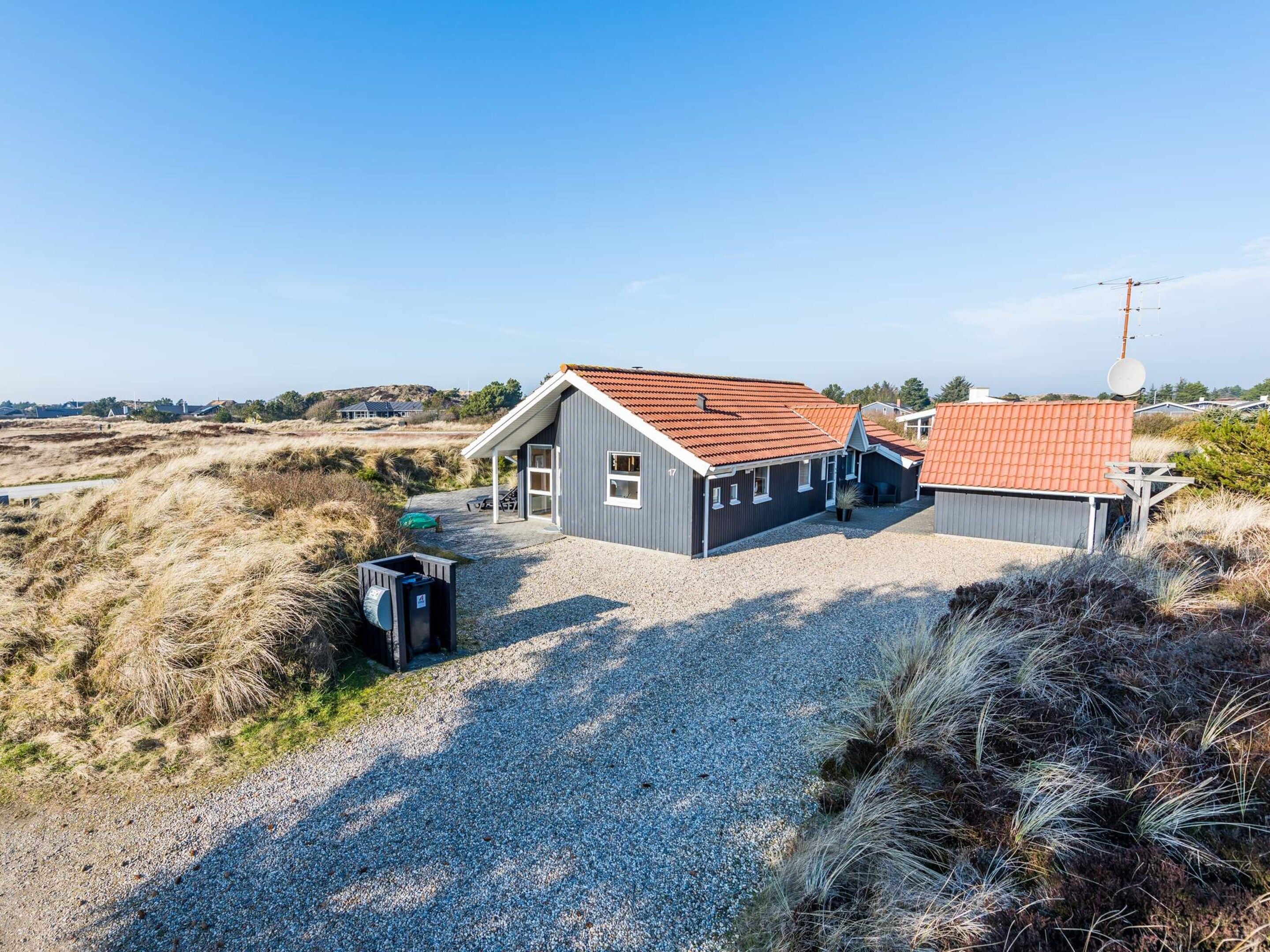 A two-story building with a red-tiled roof, a gravel driveway, and a small outdoor seating area.