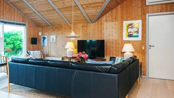 Ein modernes Wohnzimmer mit einer schwarzen Couch, Holzwänden, einem Fernseher und einem Gemälde.