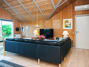 A modern living room with a black sofa, wooden walls, a TV, and a painting. - 4 Star Holiday Home in Henne (Henne)