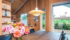 A wooden interior with a dining table, a vase of flowers, and a large window with a view of greenery. - 4 Star Holiday Home in Henne (Henne)
