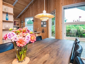 A wooden interior with a dining table, a vase of flowers, and a large window with a view of greenery. - 4 Star Holiday Home in Henne (Henne)