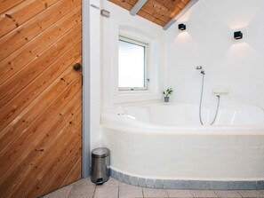 Une salle de bain moderne avec une grande baignoire, une fenêtre et une petite plante en pot.