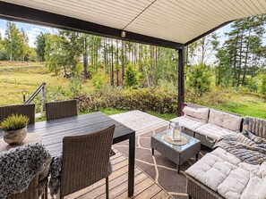 An outdoor patio with a table and chairs, a sofa, and a view of a forested area. - 5 Person Holiday Home in Mellosa (Flen)