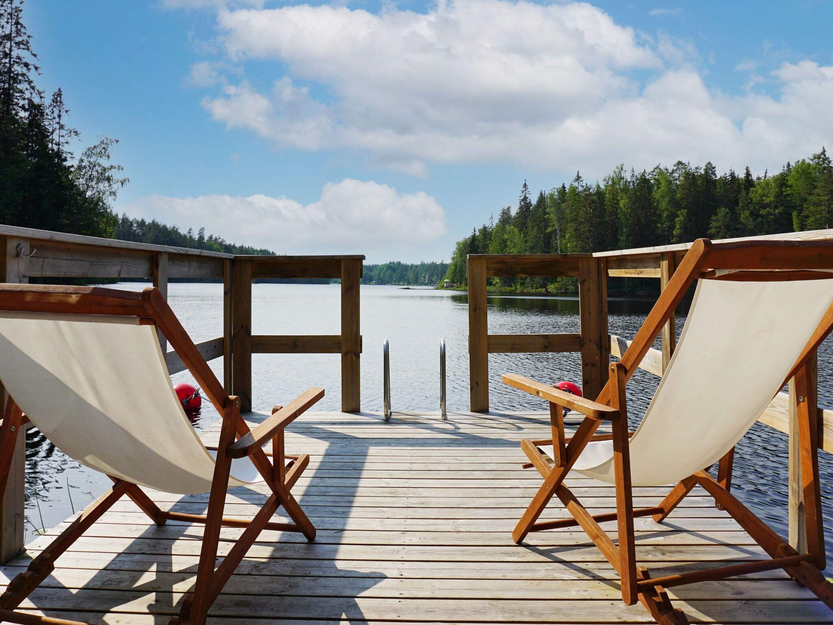 A wooden deck with two canvas chairs facing a calm lake, surrounded by trees.
