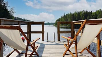 A wooden deck with two canvas chairs facing a calm lake, surrounded by trees.