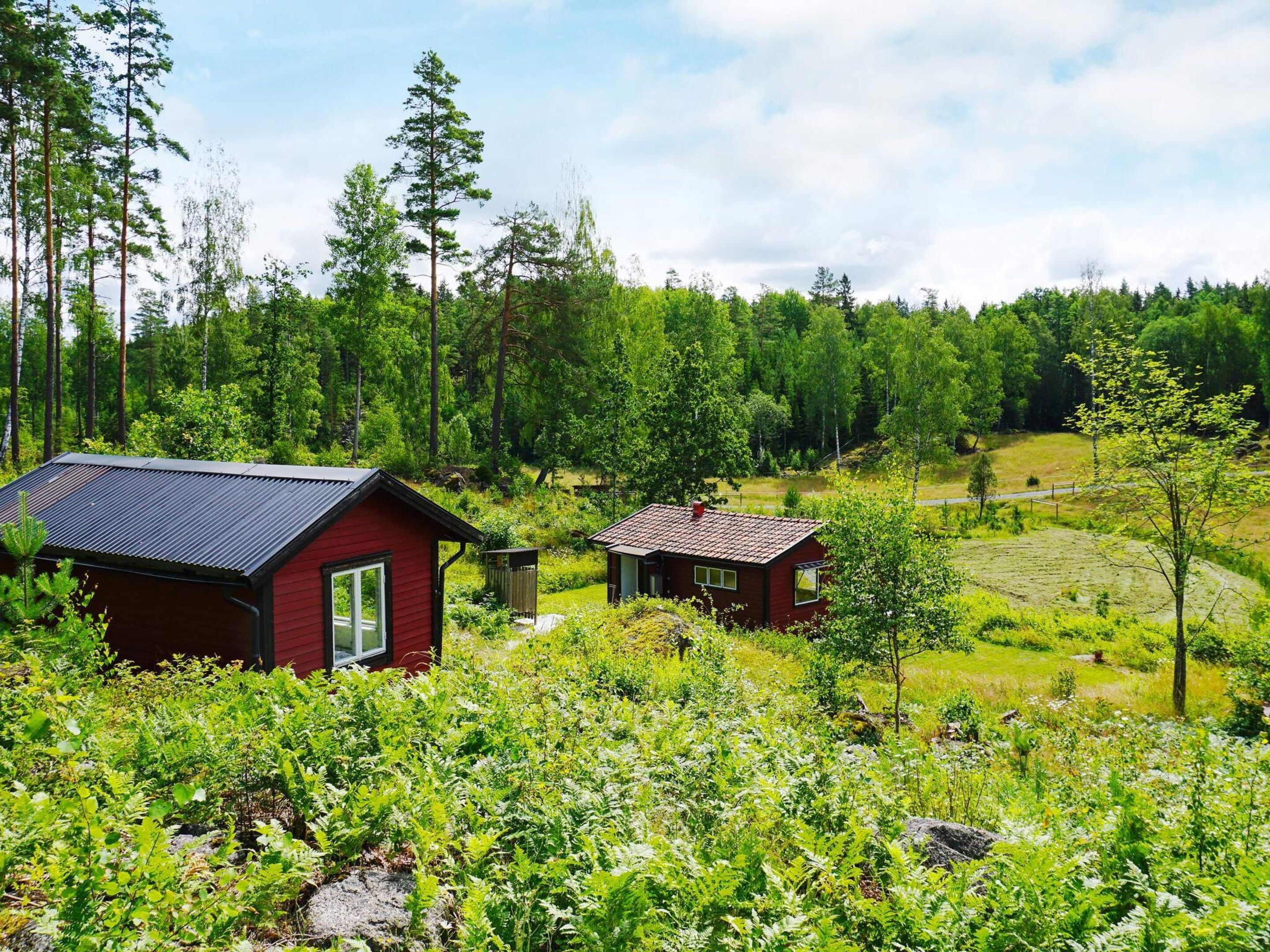 A red cabin with a metal roof, surrounded by lush greenery and trees.