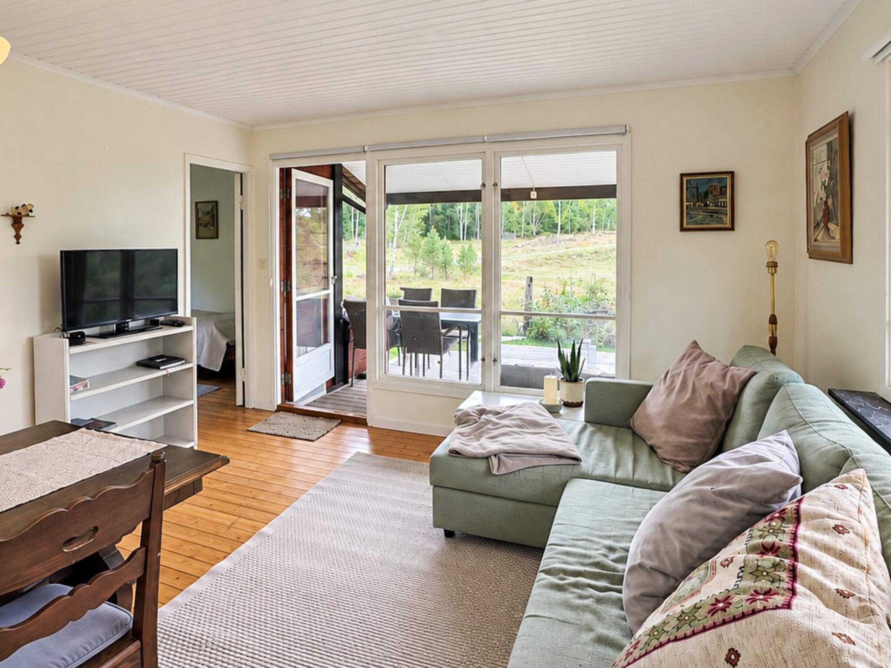 A living room with a television, a sofa, a dining table, and a sliding glass door leading to an outdoor patio.