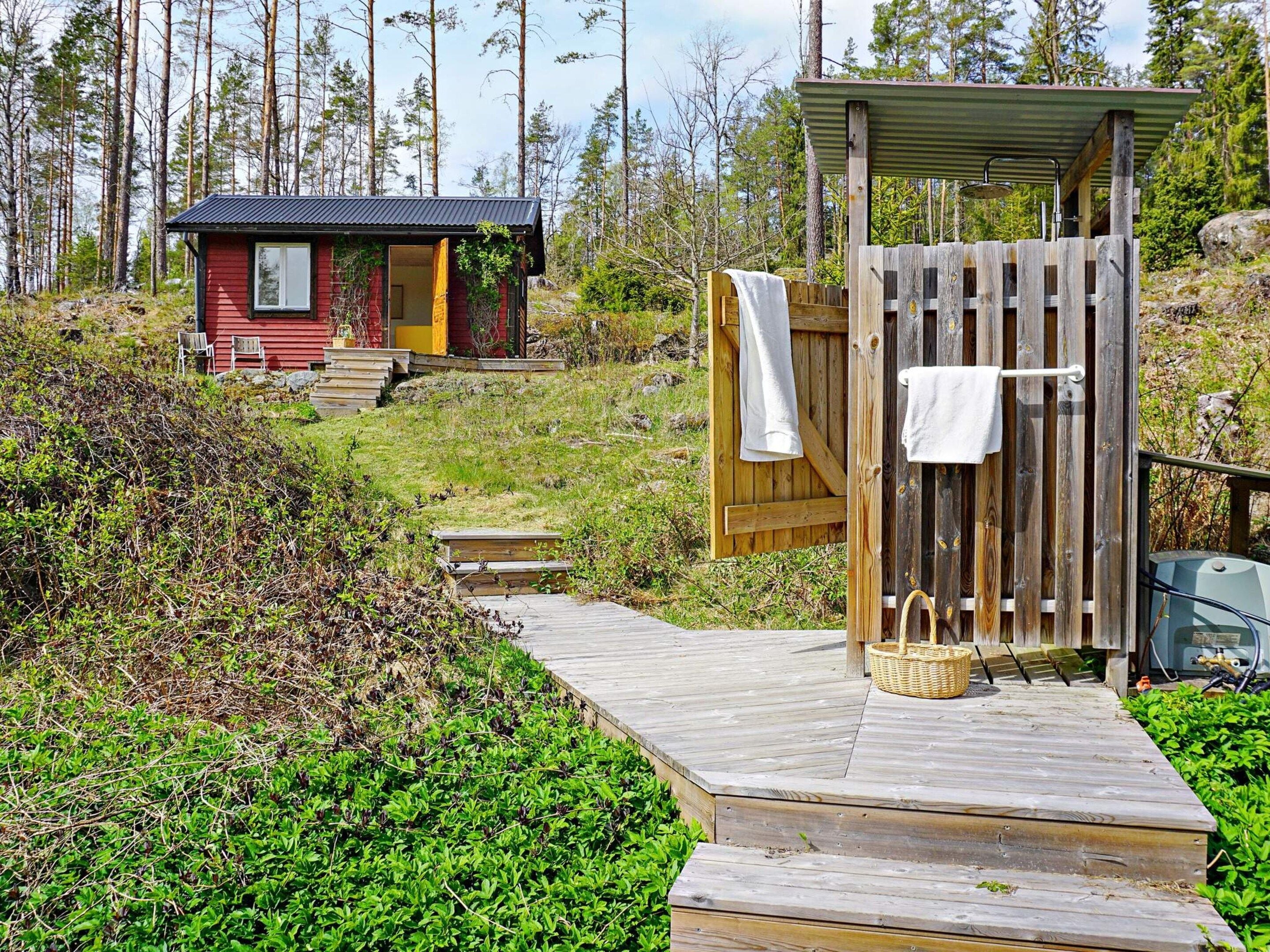 Une terrasse en bois mène à un chalet rustique à l’extérieur rouge, avec une petite construction en bois abritant une douche.