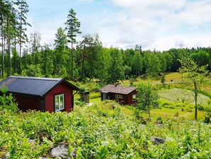 A red cabin with a metal roof, surrounded by lush greenery and trees. - 5 Person Holiday Home in Mellosa (Flen)