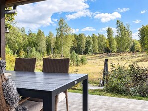 An outdoor dining area with a table and chairs, overlooking a natural landscape with trees and a grassy hill. - 5 Person Holiday Home in Mellosa (Flen)