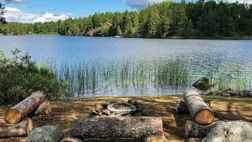 A lakeside cabin with a fire pit surrounded by logs, a clear view of the lake, and a forested backdrop.