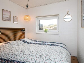 A bedroom with a wooden slat headboard, a floral-patterned bedspread, a hanging light fixture, a window with a view of the outdoors, and a wall-mounted mirror. - 4 Star Holiday Home in Hvide Sande (Hvide Sande)