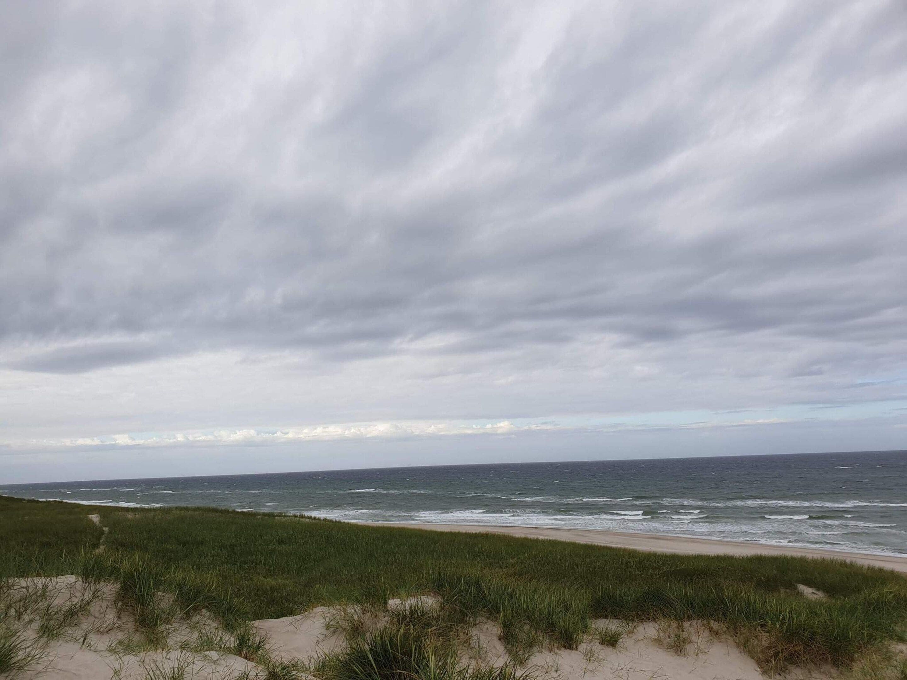Ein Strand mit Dünen und einem bewölkten Himmel.