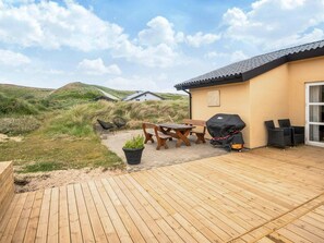 A wooden deck with outdoor furniture, a barbecue grill, and a view of the surrounding landscape.