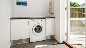 Un lavadero pequeño con lavadora Siemens, armarios blancos y una ventana.