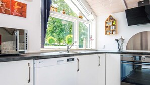Una cocina moderna con armarios blancos, horno empotrado, microondas y ventana con vistas al verdor.