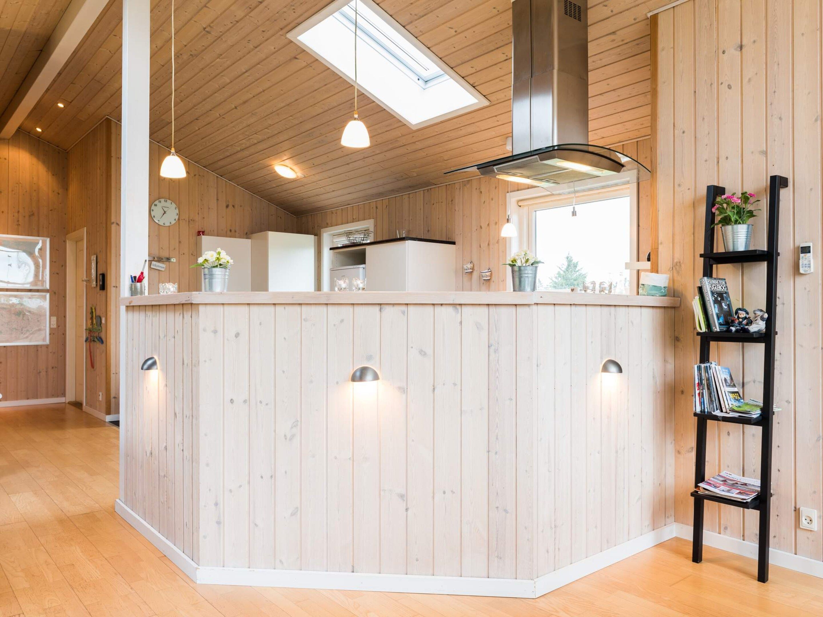 A kitchen with wooden paneling, pendant lighting, a stainless steel range hood, and a window with a view.