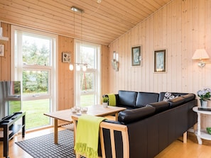 A cozy room with a wooden ceiling, a black leather sofa, a wooden table, and large windows.