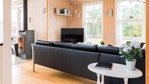 Ett modernt vardagsrum med en svart lädersoffa, en öppen spis, en tv och ett fönster med utsikt över grönområden.