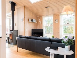 A modern living room with a black leather sofa, a fireplace, a television, and a window with a view of greenery.