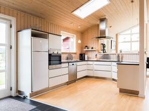 A modern kitchen with wooden paneling, a built-in oven, a dishwasher, and a large window providing natural light.