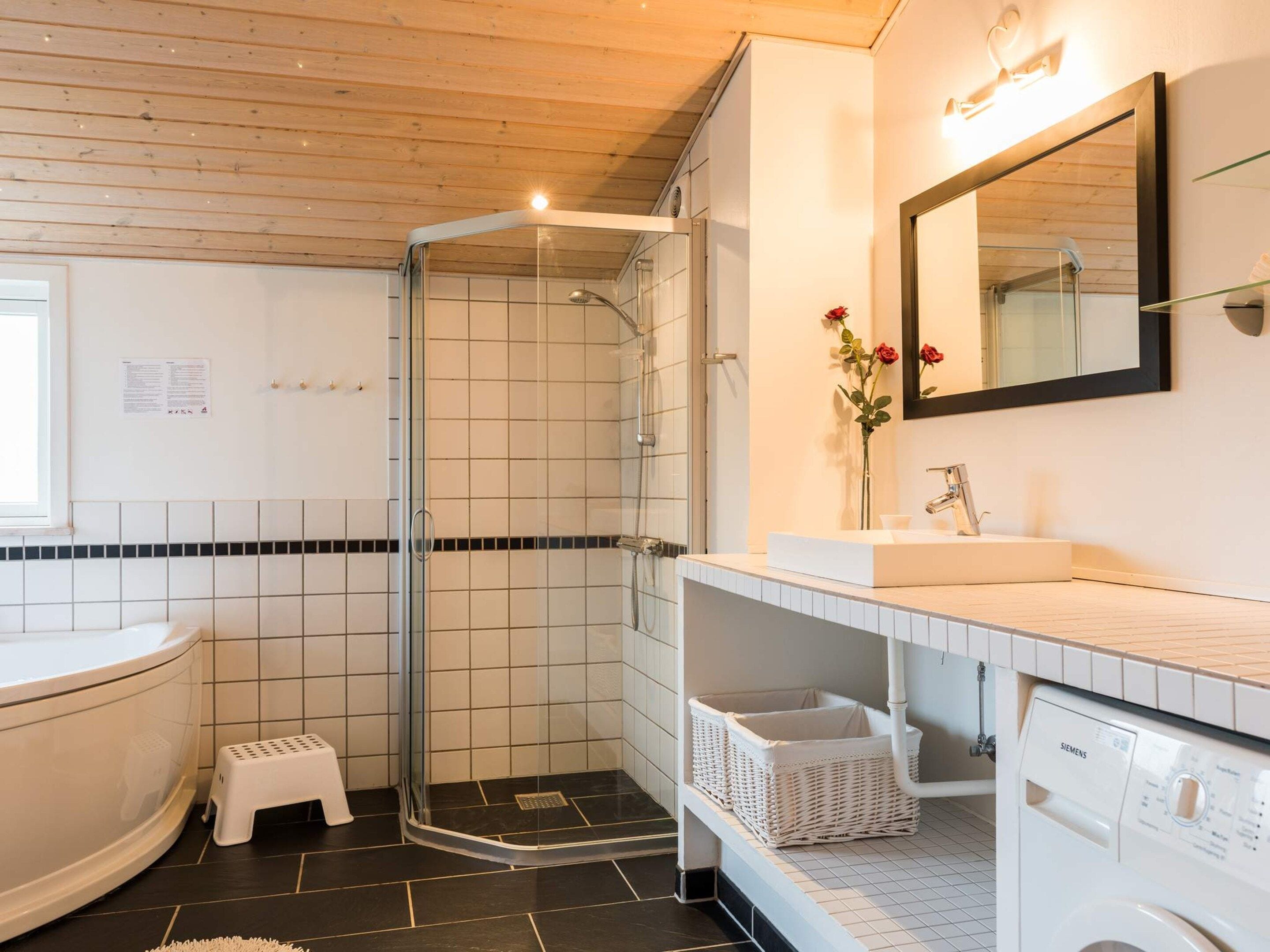 Ein modernes Badezimmer mit einer gläsernen Duschkabine, einem weißen Waschbecken und einer integrierten Waschmaschine.