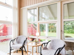 A room with two chairs and a table, large windows, and a view of a red staircase outside.