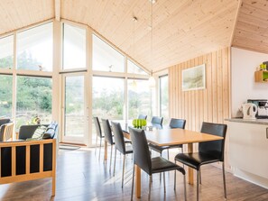 A modern dining area with a wooden table and chairs, large windows, and a view of greenery. - 5 Star Holiday Home in Norre Nebel (Norre Nebel)
