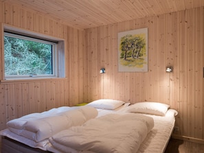 A room with wooden panel walls, a bed with white bedding, a window with a view of trees, and a painting of trees on the wall. - 5 Star Holiday Home in Norre Nebel (Norre Nebel)