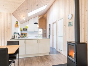 A modern kitchen with white cabinets, a black stove, and a dining area with a table and chairs. - 5 Star Holiday Home in Norre Nebel (Norre Nebel)