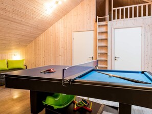A ping pong table with a net, a ball, and paddles in a room with wooden walls and a ladder leading to a door. - 5 Star Holiday Home in Norre Nebel (Norre Nebel)