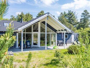 A modern house with a covered patio, large windows, and a well-maintained lawn. - 5 Star Holiday Home in Norre Nebel (Norre Nebel)
