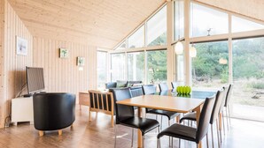 Un comedor moderno con una mesa y sillas de madera, ventanas amplias y vistas a espacios verdes.