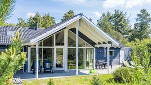 Una casa moderna con un amplio patio cubierto de vidrio, una zona de estar al aire libre techada y un césped bien cuidado.