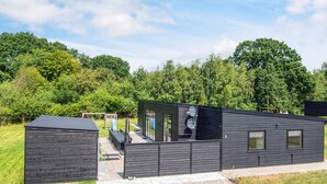 Un bâtiment moderne à l’extérieur noir, doté d’un patio couvert et d’une aire de jeux en arrière-plan.