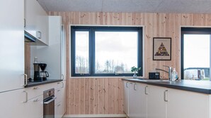 Une cuisine moderne avec des murs recouverts de panneaux en bois, une grande fenêtre et une machine à café posée sur le plan de travail.