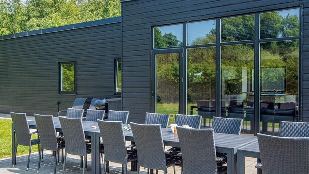 Un espace de restauration en plein air doté de nombreuses tables et chaises, de grandes fenêtres et d’une façade de bâtiment moderne.