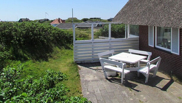 A patio area with a table and benches, a thatched-roof house, and a view of the surrounding landscape. - 6 Person Holiday Home in Fano (Fano)