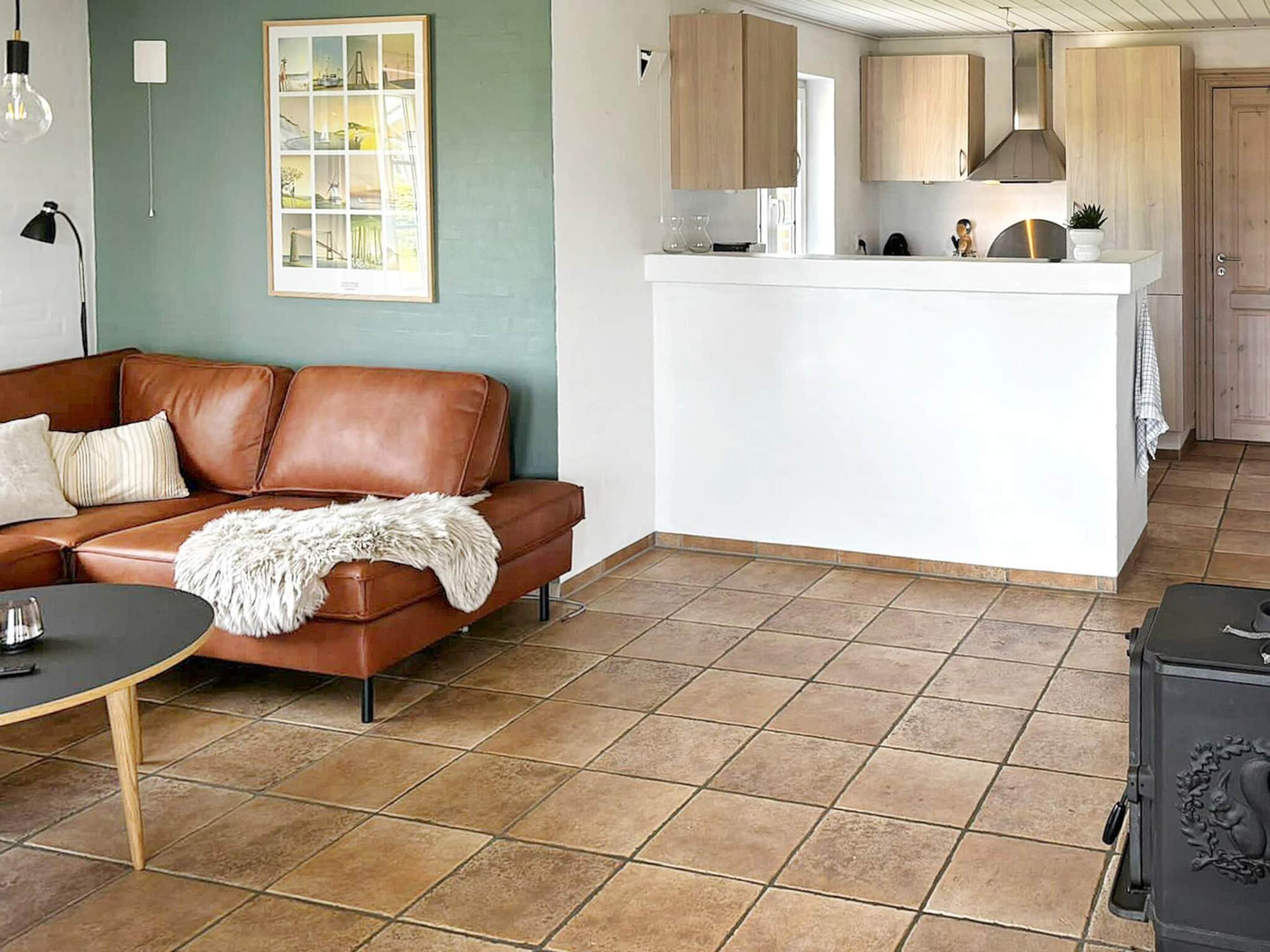A compact living space with a brown leather sofa, a small round table, and a kitchen area with wooden cabinets and a white countertop.