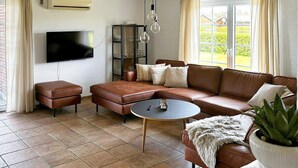 Uma sala de estar com um sofá de couro marrom, uma mesa de centro pequena, uma televisão e uma estante de livros.