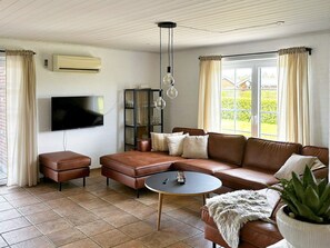 A living room with a brown leather sofa, a small round coffee table, a television mounted on the wall, and a potted plant. - 4 Star Holiday Home in Tarm (Tarm)