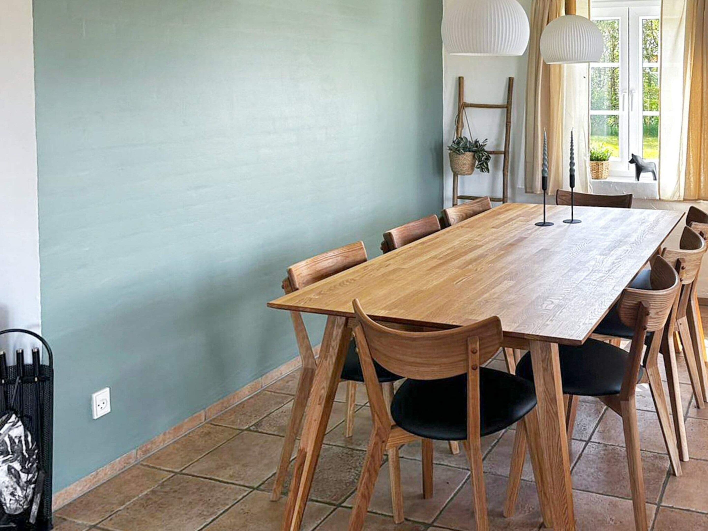 A dining area with a wooden table and chairs, a hanging plant, and a window with curtains.