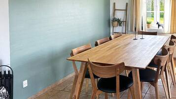 A dining area with a wooden table and chairs, a hanging plant, and a window with curtains.