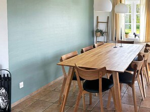 A dining area with a wooden table and chairs, a hanging plant, and a window with curtains. - 4 Star Holiday Home in Tarm (Tarm)