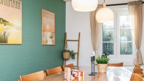 Uma sala de jantar com mesa de madeira, cadeiras, luminárias pendentes e uma janela com cortinas.